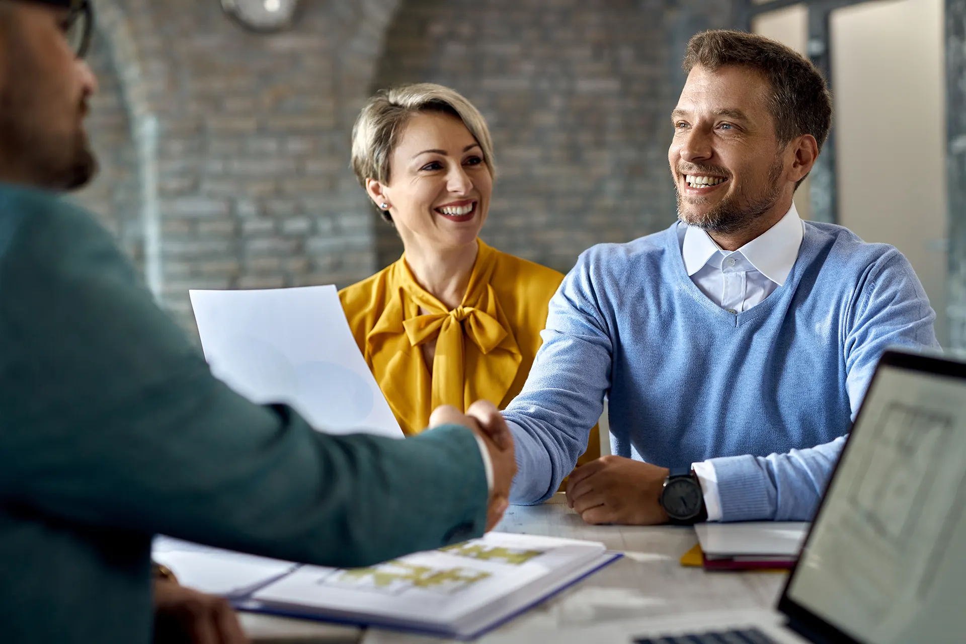 happy-couple-shaking-hands-with-real-estate-agent-after-successful-agreement-office